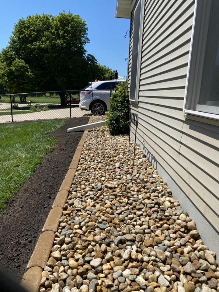 Rock landscaping along a house's exterior with a clear blue sky and parked car in the background.