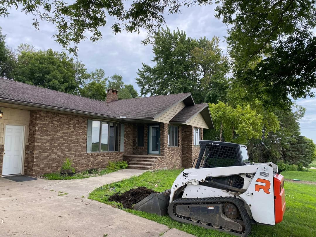 House with brown brick exterior and a Bobcat excavator parked on a driveway.