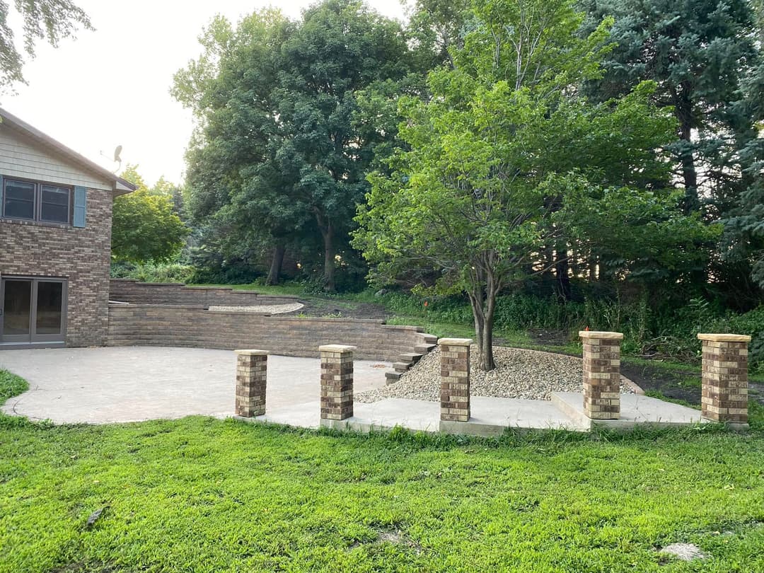 Backyard landscape with brick patio, stairs, trees, and greenery, creating a serene outdoor space.
