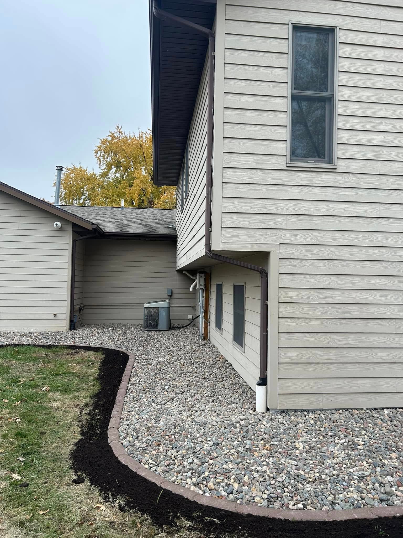 Exterior view of a house corner with landscaped gravel, mulch edging, and an air conditioning unit.